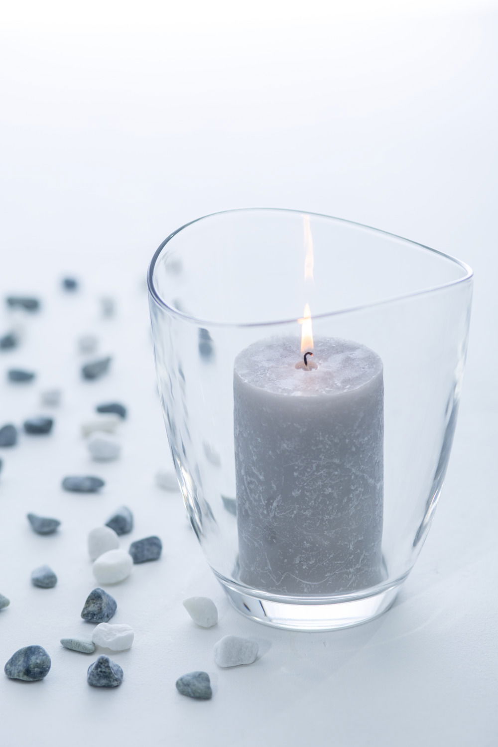 Windlicht LOOP 16,8 cm mit brennender Kerze, umgeben von kleinen Steinen, aus seitlicher Perspektive fotografiert.
