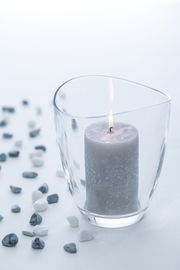 Windlicht LOOP 16,8 cm mit brennender Kerze, umgeben von kleinen Steinen, aus seitlicher Perspektive fotografiert.