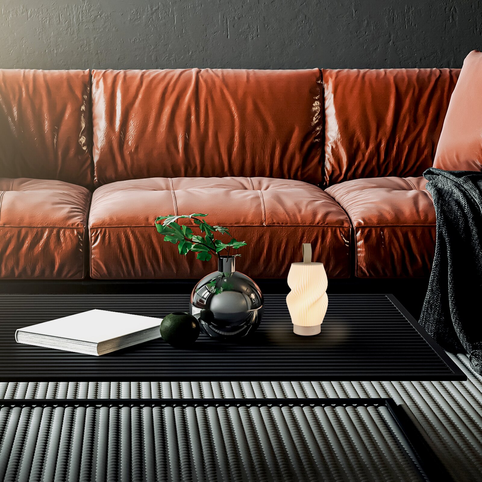 Moderne, kleine Tischlampe mit gedrehtem, geriffeltem Schirm in warmweißem Licht auf schwarzem Couchtisch vor braunem Ledersofa, Frontansicht aus leicht erhöhter Perspektive.