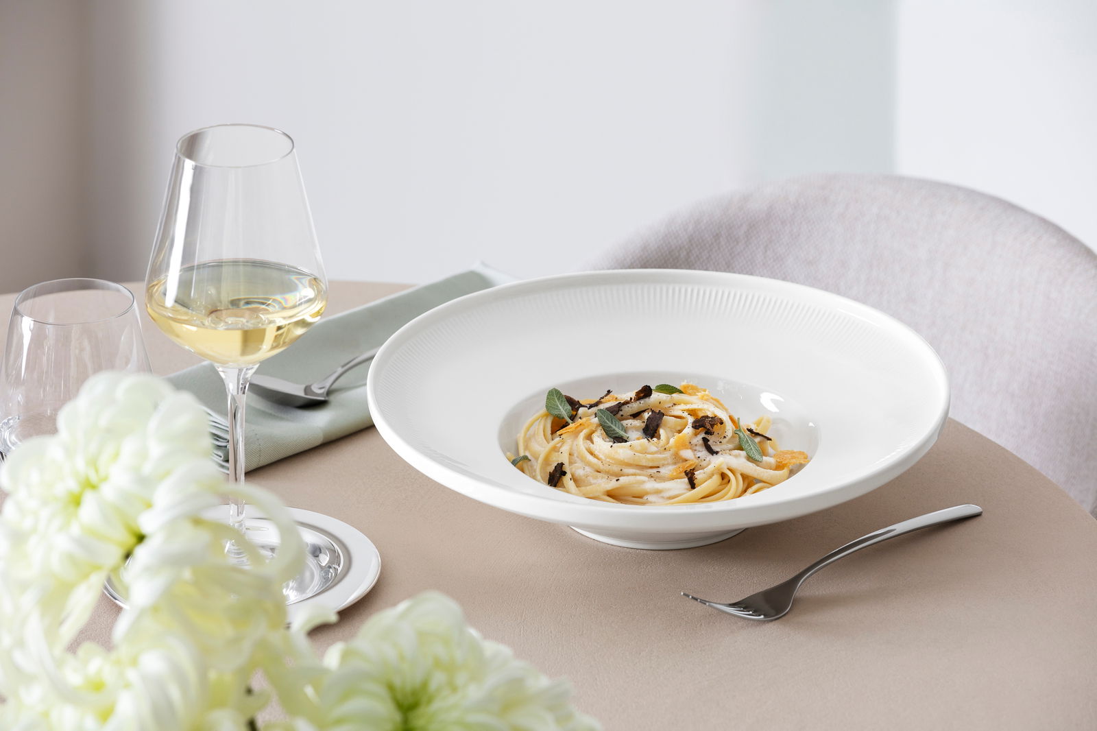 Eleganter weißer Suppenteller Afina mit 29,2 cm Durchmesser, gefüllt mit Pasta, auf einem gedeckten Tisch mit Weinglas und Blumen, seitliche Perspektive.