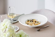 Elegant wit soepbord Afina met een diameter van 29,2 cm, gevuld met pasta, op een gedekte tafel met een wijnglas en bloemen, zijaanzicht.