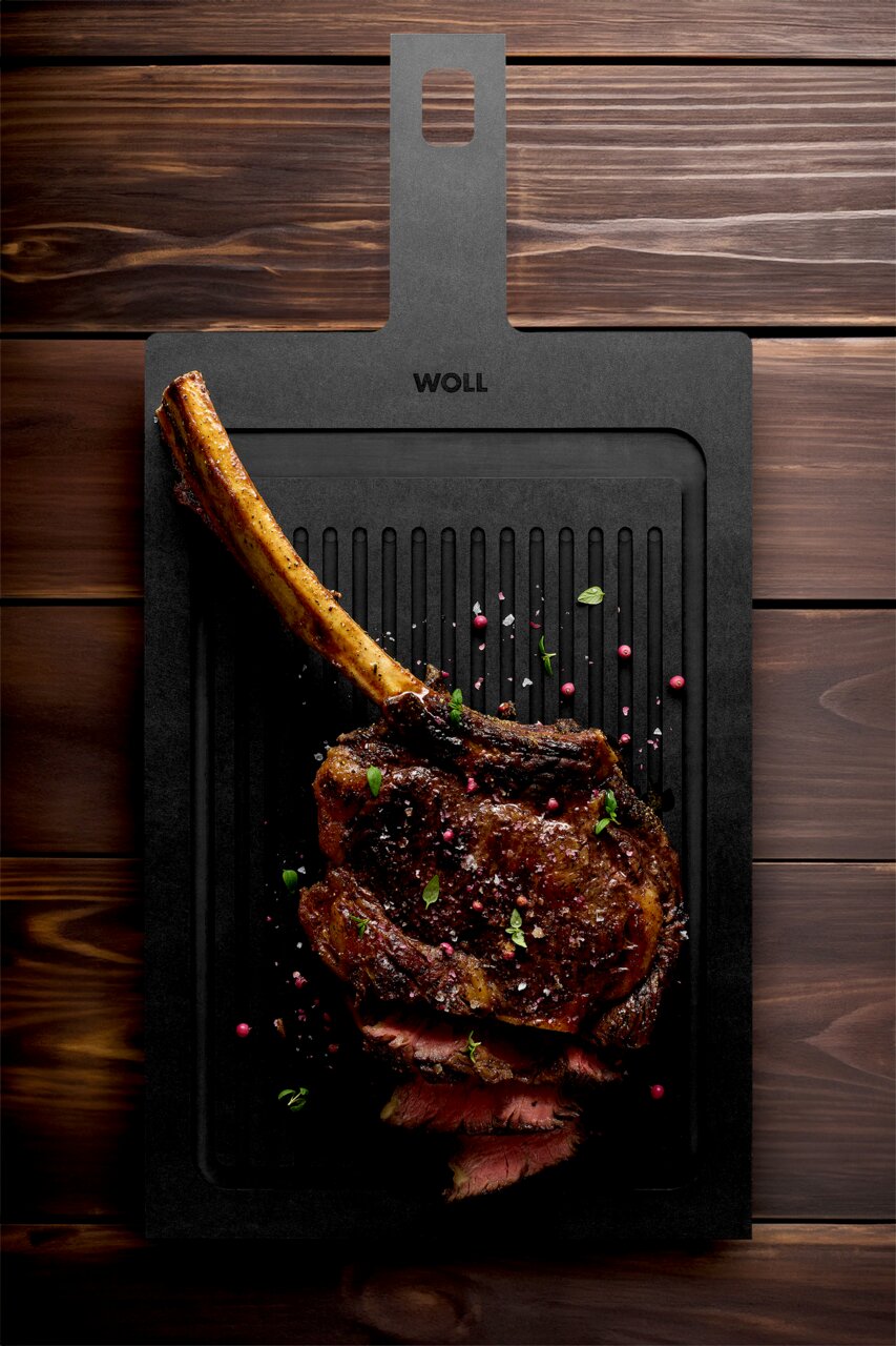 Snijplank met groeven, met daarop een sappige, gegrilde tomahawk-steak met kruiden, gefotografeerd vanuit vogelperspectief.