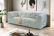 Modernes, hellgraues Stoffsofa mit gepolsterter Kassetten-Steppung in einem minimalistischen Wohnzimmer, schräg von vorne aus leicht erhöhter Perspektive fotografiert