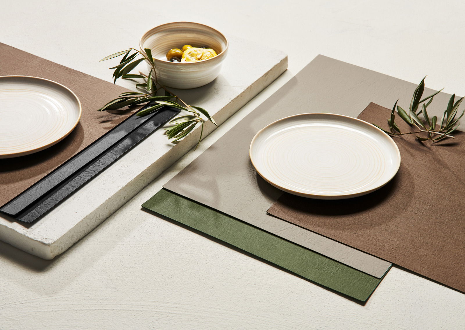 ASA SELECTION Tischset CLAY Tischset in verschiedenen Farben, darunter Braun, Grau und Grün, mit einem Teller und einer Schale, dekoriert mit Olivenzweigen, aus der Vogelperspektive fotografiert.