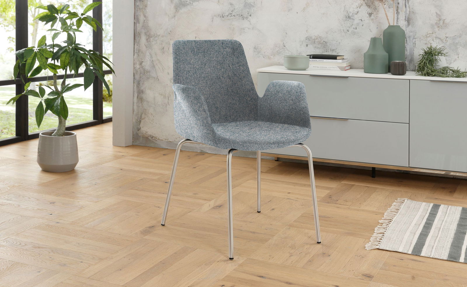 Moderner Besuchersessel mit blaugrauem Stoffbezug und schlanken Metallbeinen, seitliche Perspektive