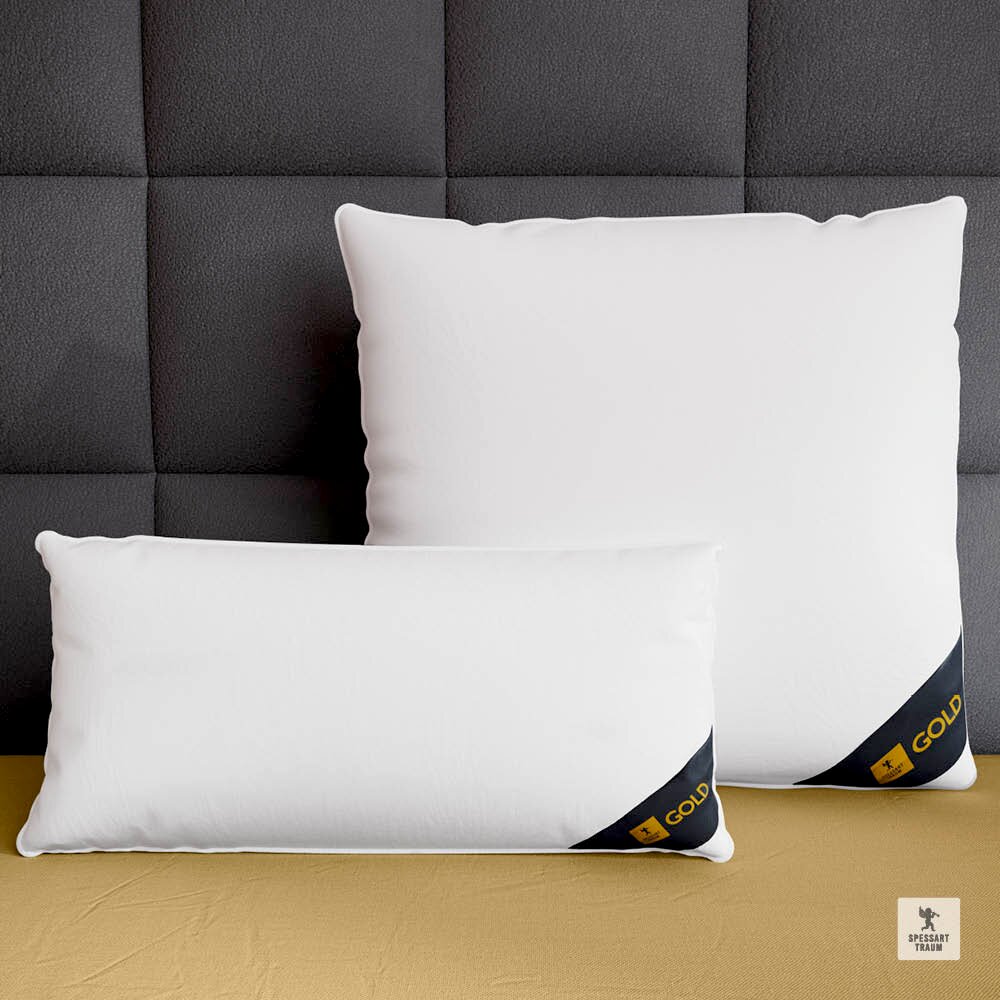 Spessarttraum Kissen GOLD Zwei weiße Spessarttraum Kissen GOLD in den Größen 80x80cm und 40x80cm, frontal auf einem goldfarbenen Bett vor einer grauen, gepolsterten Wand platziert.