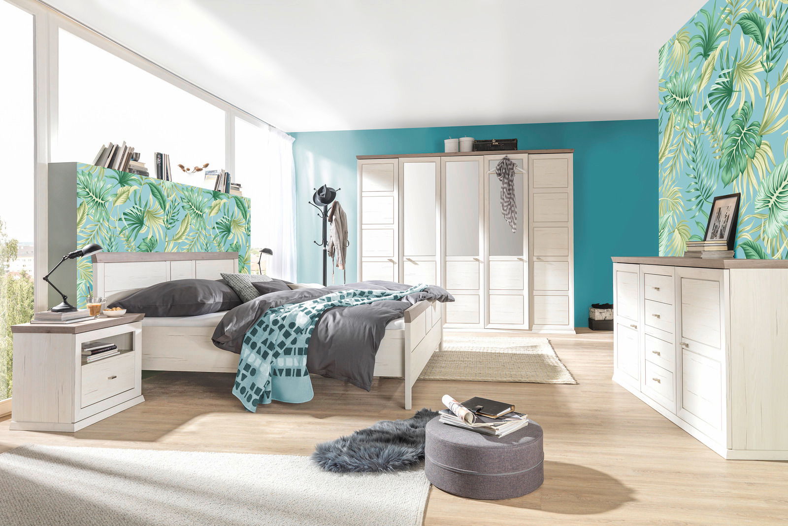 Helles Schlafzimmer mit einem 5-türigen Drehtürenschrank, einem großen Bett, einer Nachtkommode und einem Sideboard in Holzoptik. Die Perspektive zeigt den Raum von der Seite mit Blick auf das Bett und den Schrank.