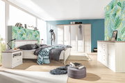 Helles Schlafzimmer mit einem 5-türigen Drehtürenschrank, einem großen Bett, einer Nachtkommode und einem Sideboard in Holzoptik. Die Perspektive zeigt den Raum von der Seite mit Blick auf das Bett und den Schrank.