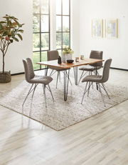 Moderner Esstisch mit Holzplatte und Metallbeinen, umgeben von vier grauen Stühlen auf einem Teppich, in einem hellen Raum mit großen Fenstern, seitliche Perspektive.