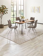 Moderner Esstisch mit Holzplatte und Metallbeinen, umgeben von vier grauen Stühlen auf einem Teppich, in einem hellen Raum mit großen Fenstern, seitliche Perspektive.