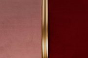 Nahaufnahme eines Hockers mit zweifarbiger Polsterung in Rosa und Rot, getrennt durch einen goldenen Streifen in der Mitte.