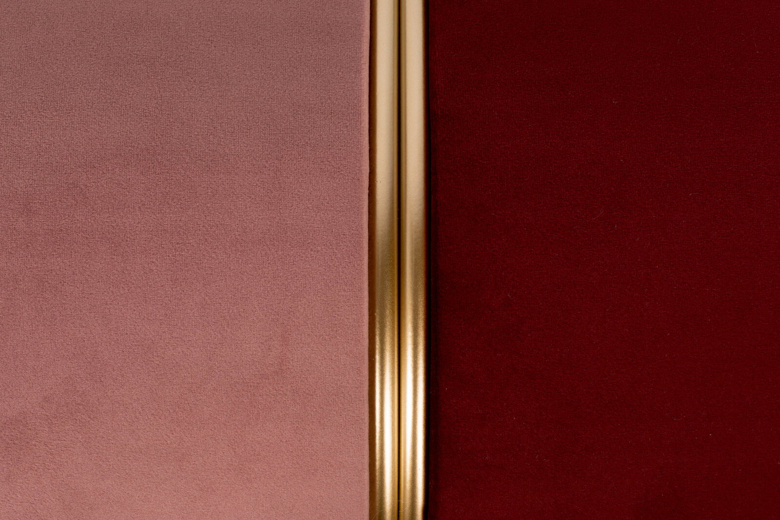 Nahaufnahme eines Hockers mit zweifarbiger Polsterung in Rosa und Rot, getrennt durch einen goldenen Streifen in der Mitte.