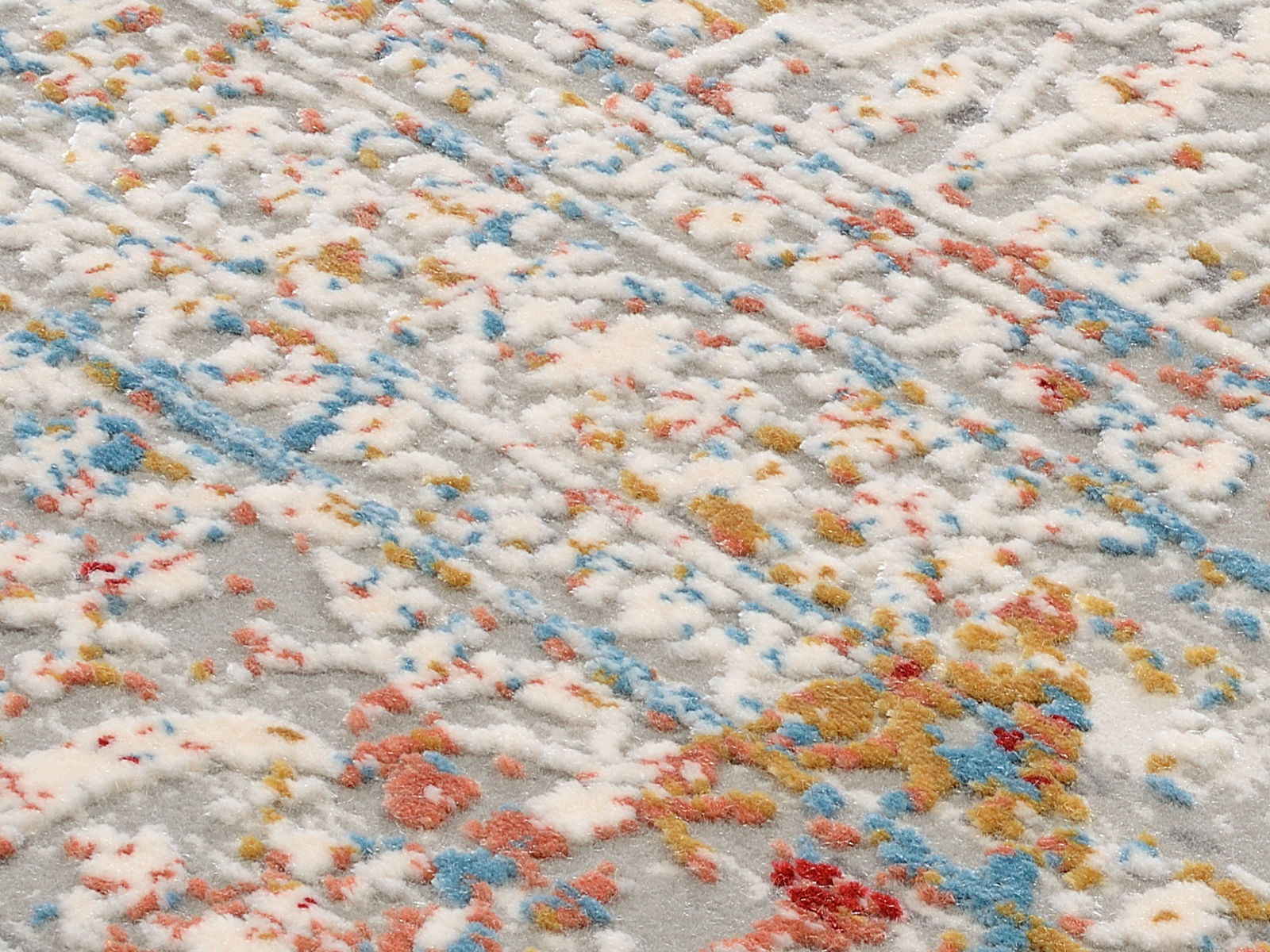 Nahaufnahme eines Designer-Teppichs mit buntem, abstraktem Muster in Weiß, Blau, Rot und Gelb. Die Perspektive zeigt die Textur und das Detail des Teppichs.