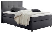 Graues Boxspringbett mit hohem Kopfteil, seitliche Perspektive, dekoriert mit Kissen und Decke.