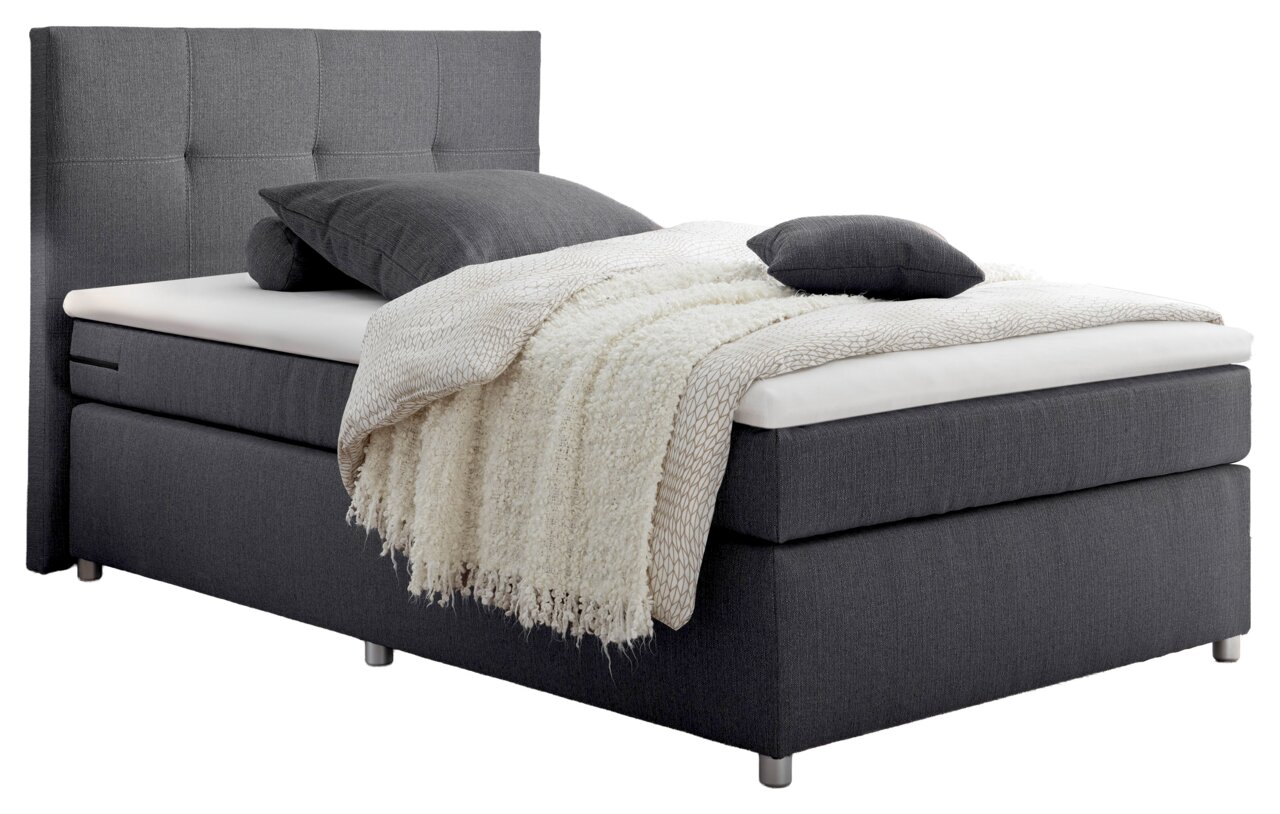 Graues Boxspringbett mit hohem Kopfteil, seitliche Perspektive, dekoriert mit Kissen und Decke.
