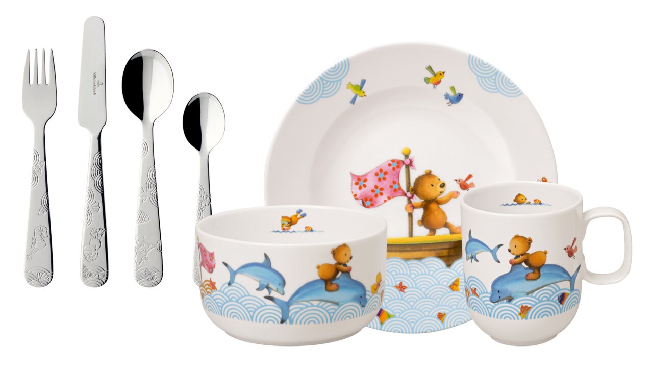 Kinder Geschirr-Set mit Bären- und Delfinmotiven, bestehend aus Teller, Schale, Tasse und Besteck, aus seitlicher Perspektive fotografiert.