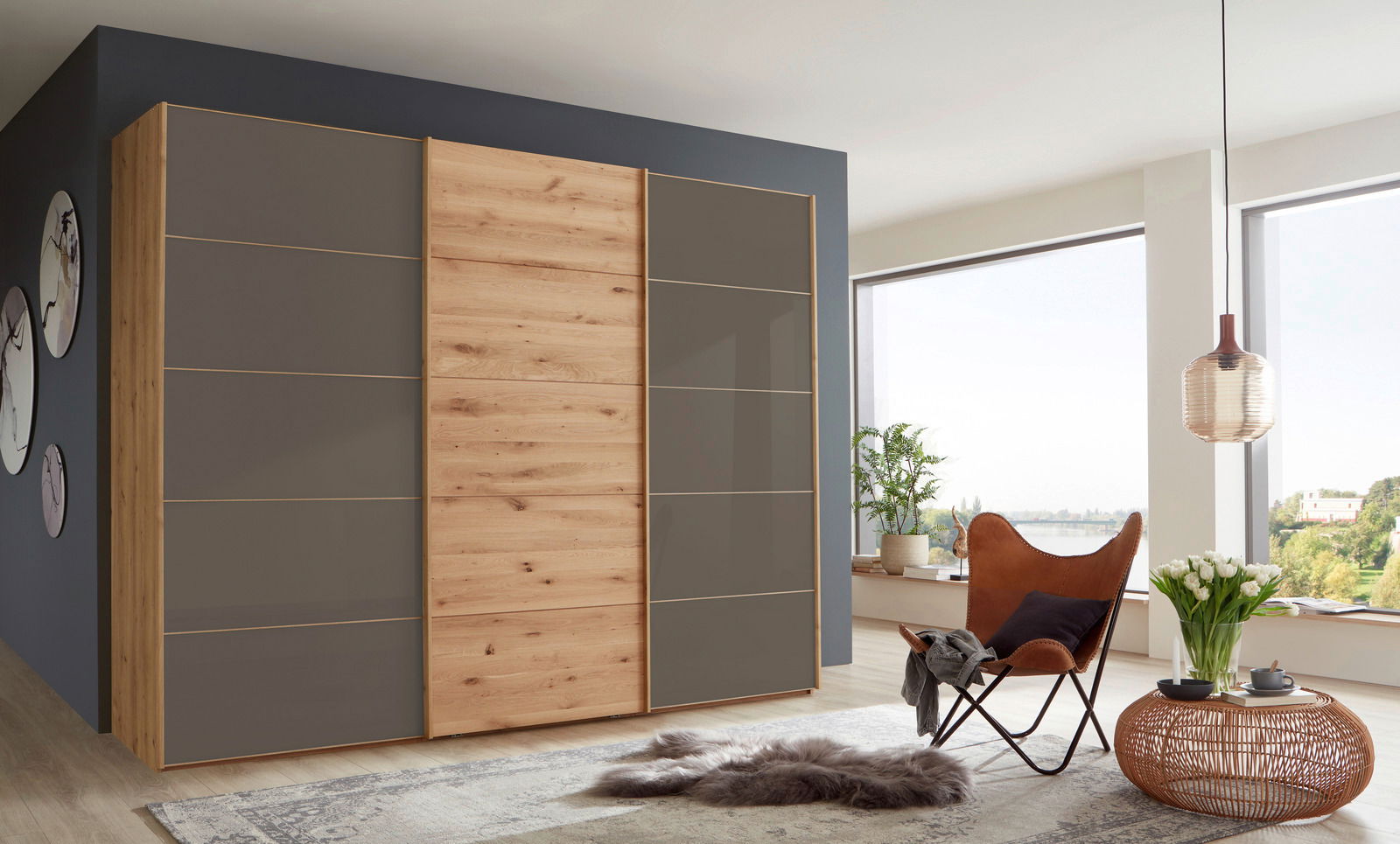 Moderner Schwebetürenschrank mit drei Türen in Holzoptik und grauen Elementen, seitliche Perspektive im stilvollen Wohnzimmer.