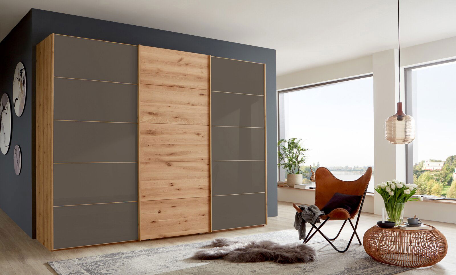 Moderner Schwebetürenschrank mit drei Türen in Holzoptik und grauen Elementen, seitliche Perspektive im stilvollen Wohnzimmer.