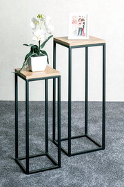 Zwei moderne Beistelltische mit schwarzem Metallrahmen und Holzoberfläche, einer mit einer weißen Orchidee und der andere mit einem Bilderrahmen, aus seitlicher Perspektive fotografiert.