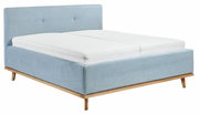 Stoffen bed met lichtblauwe bekleding en houten poten, zijaanzicht