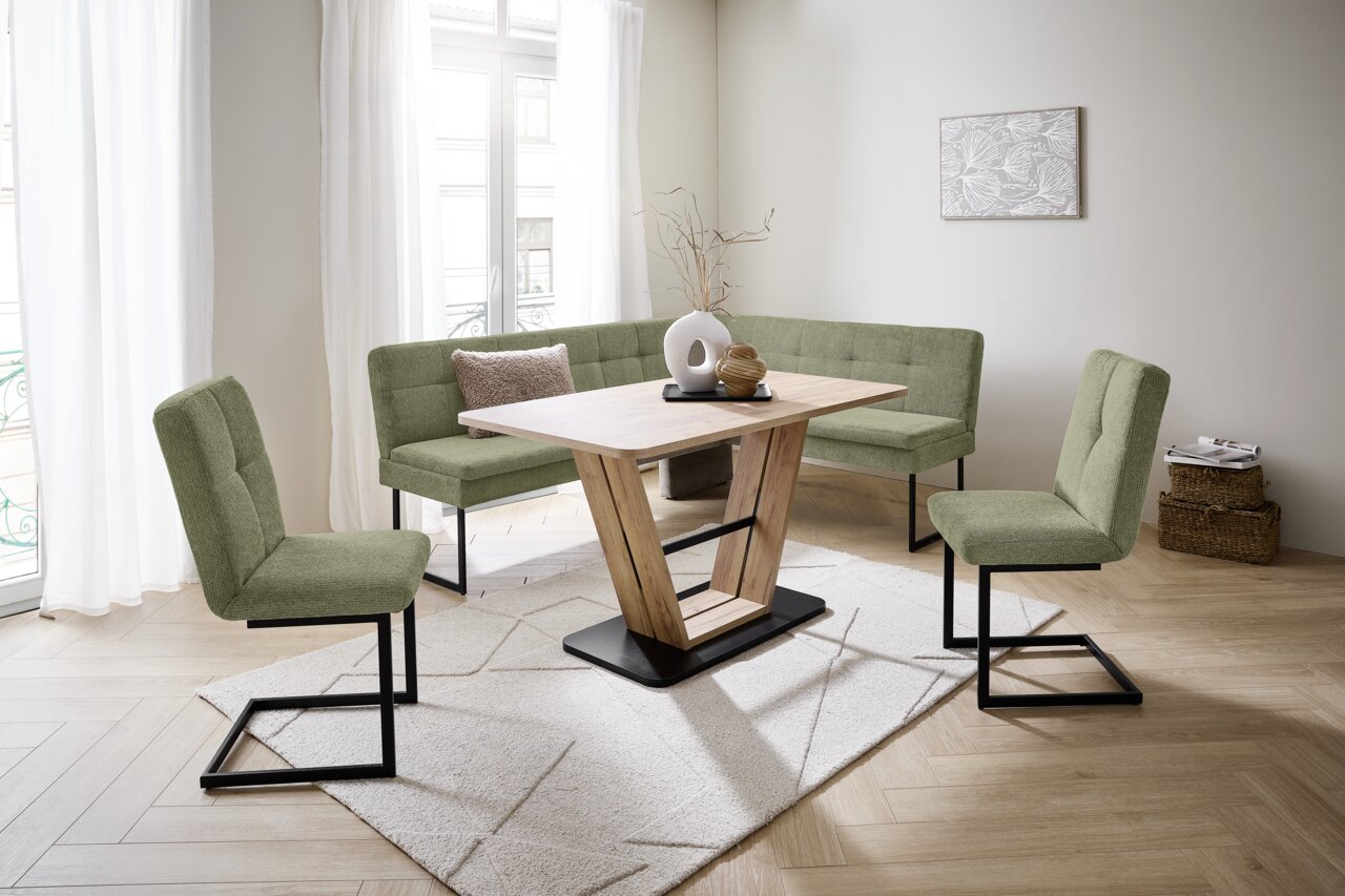 Novel Schommelstoel QUICK Moderne eethoek met hoekbank en groene stoffen bekleding en een houten tafel in een lichte ruimte, gezien vanuit de zijkant.