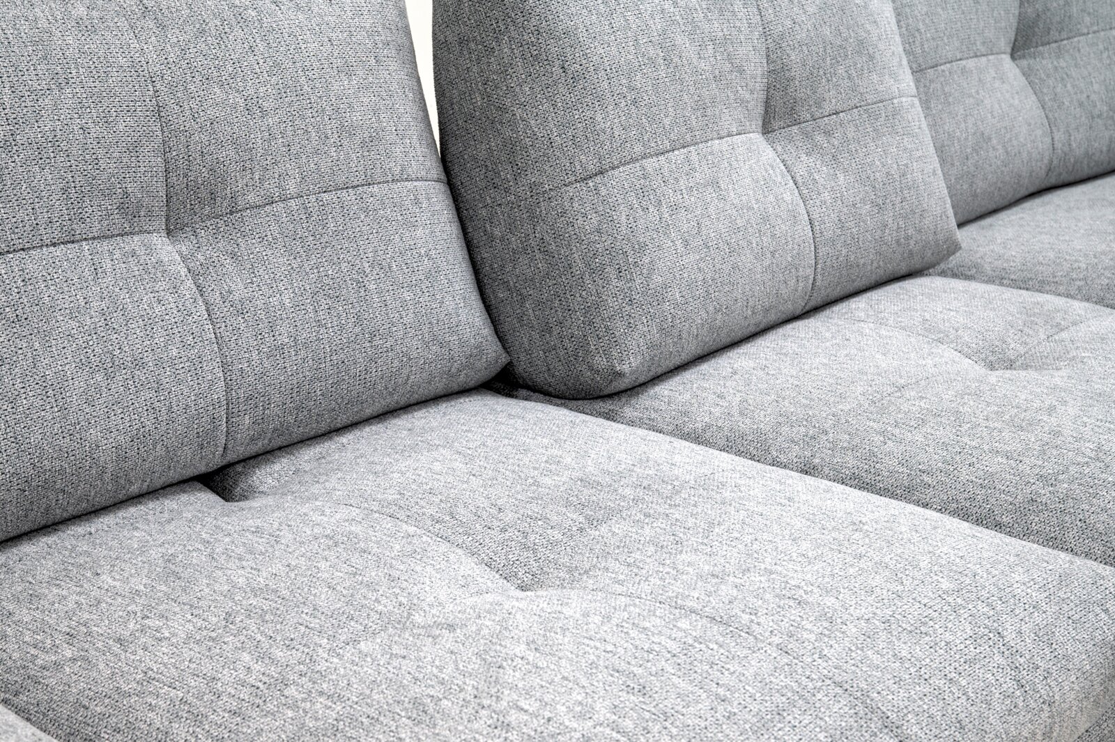 Detailaufnahme aus schräger Seitenperspektive: hellgraues Stoffsofa mit gepolsterter Sitzfläche und gesteppten Rückenlehnenpolstern