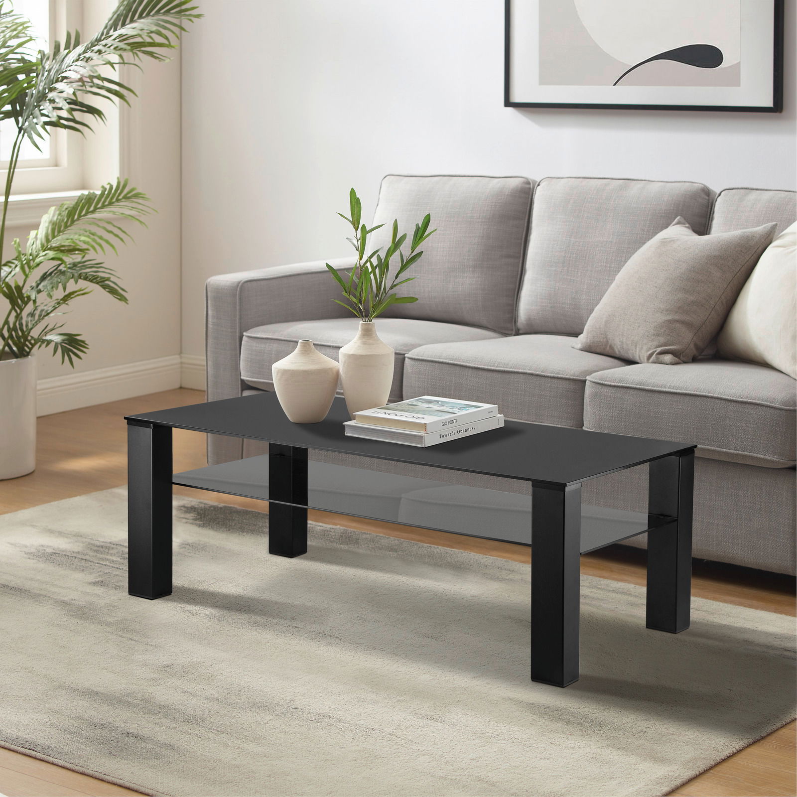 Moderner Couchtisch XORA Tisch ROMINA in schwarzem Design, frontal im Wohnzimmer mit grauem Sofa und Pflanzen im Hintergrund.