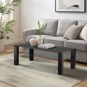 Moderner Couchtisch XORA Tisch ROMINA in schwarzem Design, frontal im Wohnzimmer mit grauem Sofa und Pflanzen im Hintergrund.