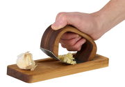 Knoblauchpresse RoccaAlio aus Holz und Metall, seitliche Perspektive, zeigt eine Hand, die Knoblauch auf einem Holzbrett presst.