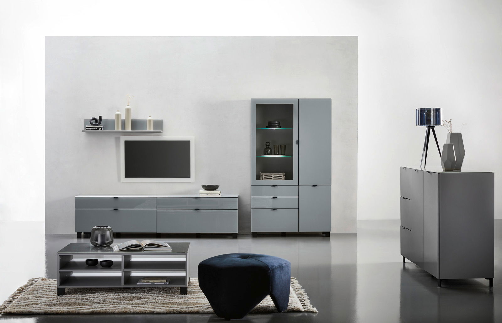 Moderne Wohnzimmermöbel in grauem Design, bestehend aus einem TV-Lowboard, einer Vitrine, einem Couchtisch und einem Sideboard, aus frontaler Perspektive.
