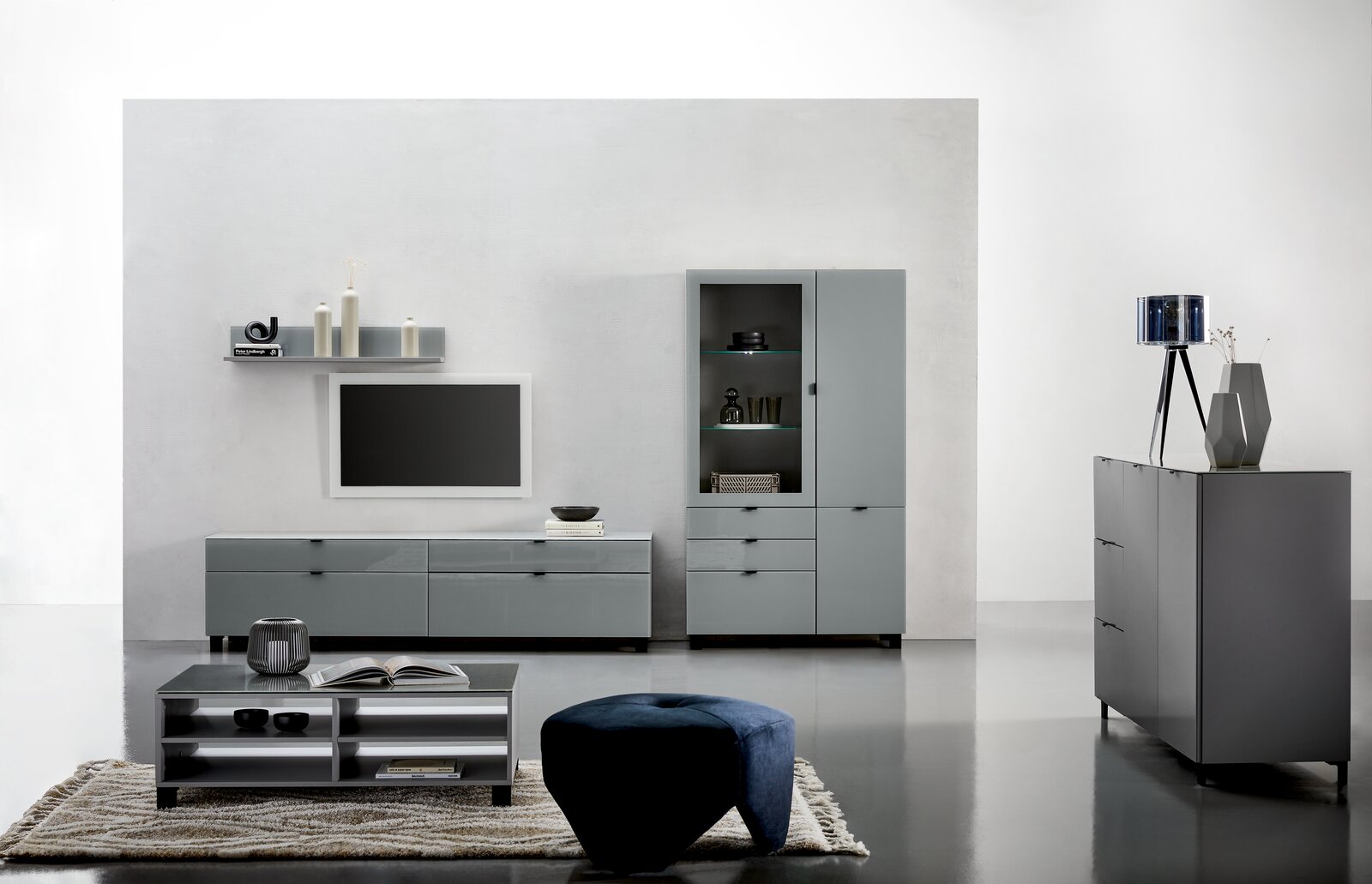 Moderne Wohnzimmermöbel in grauem Design, bestehend aus einem TV-Lowboard, einer Vitrine, einem Couchtisch und einem Sideboard, aus frontaler Perspektive.