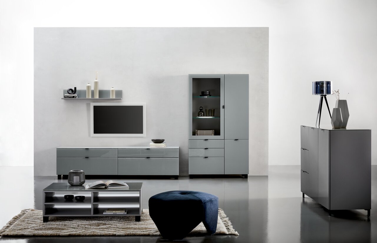 Moderne Wohnzimmermöbel in grauem Design, bestehend aus einem TV-Lowboard, einer Vitrine, einem Couchtisch und einem Sideboard, aus frontaler Perspektive.