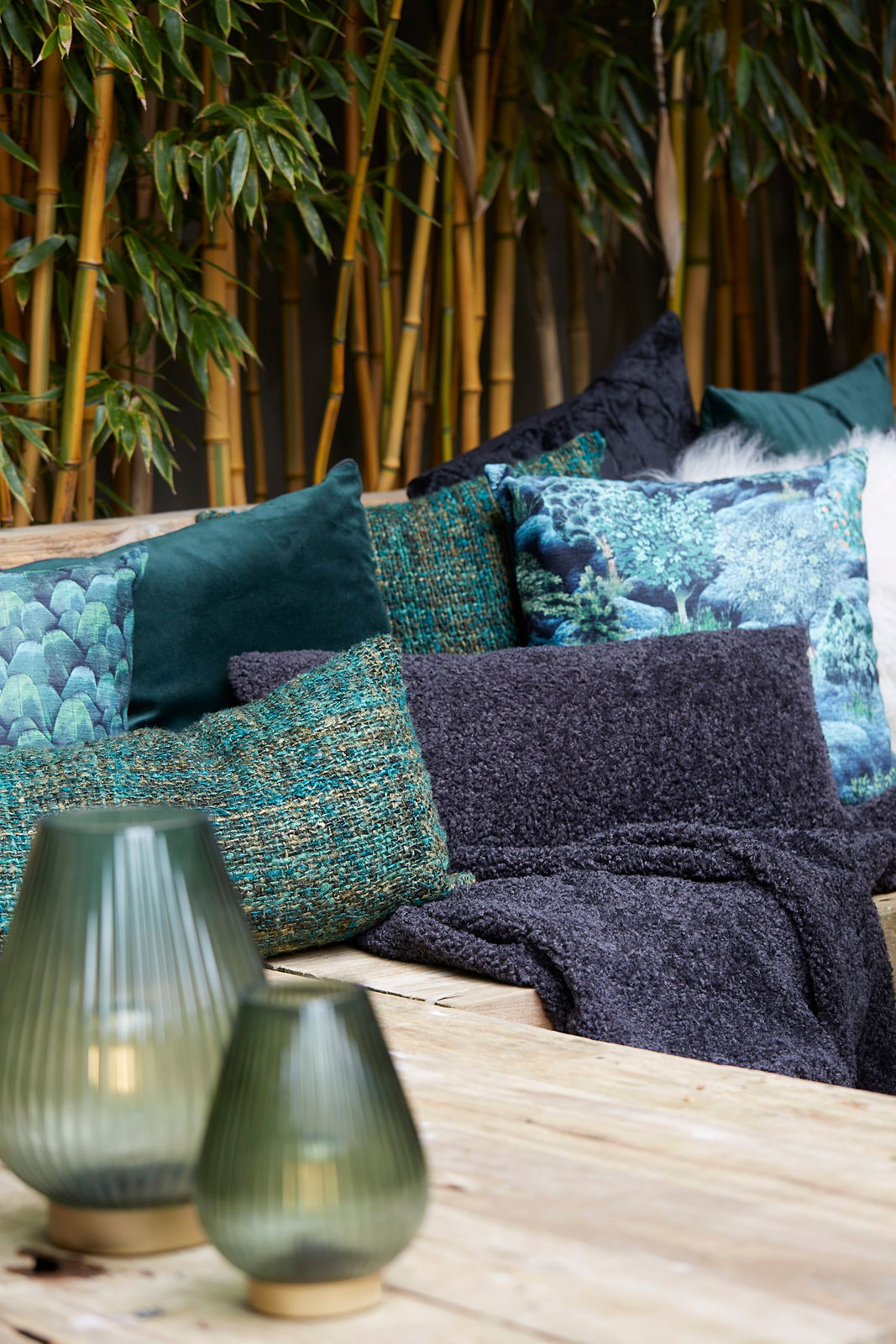 Light&Living Kissen 60x30 cm LINA dunkel gr LINA Ein dunkelgrünes Kissen 60x30 cm LINA auf einem Holztisch, umgeben von anderen dekorativen Kissen und grünen Pflanzen im Hintergrund, aus seitlicher Perspektive.