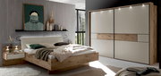 Modernes Schlafzimmer-Set mit Holzbett und gepolstertem Kopfteil, Nachttisch und großem Schwebetürenschrank in Weiß mit Holz-Akzentstreifen und LED-Spots, gezeigt in frontaler leicht seitlicher Perspektive.