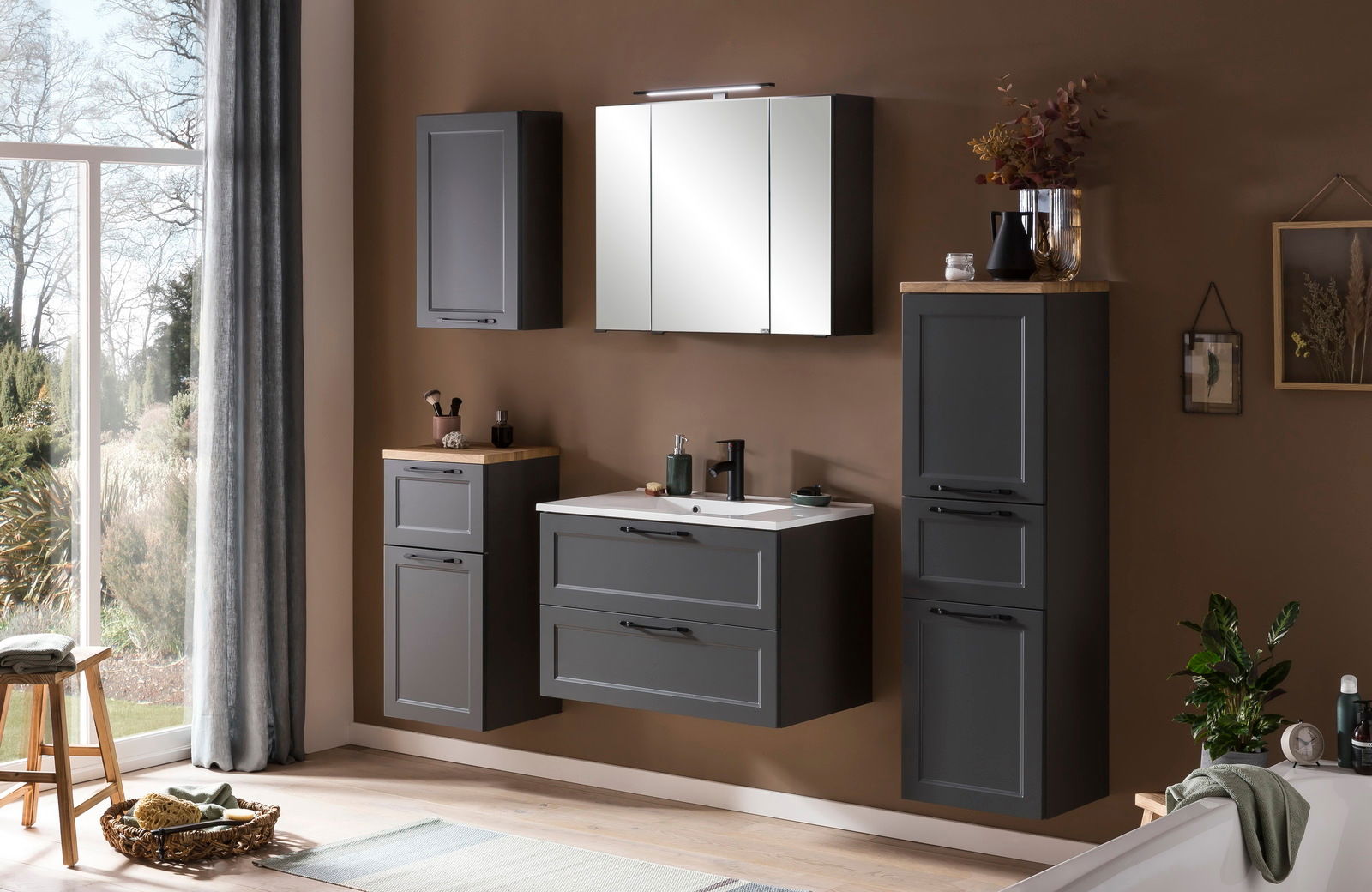 Moderne Badezimmermöbel in dunklem Grau, bestehend aus einem Unterschrank mit Waschbecken, einem hohen Schrank und einem Spiegelschrank, aus der Frontalperspektive betrachtet.