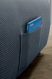 Close-up van een grijze, gestructureerde hoekbank met een handig zijvak waarin een blauw notitieboekje ligt. Zijaanzicht.