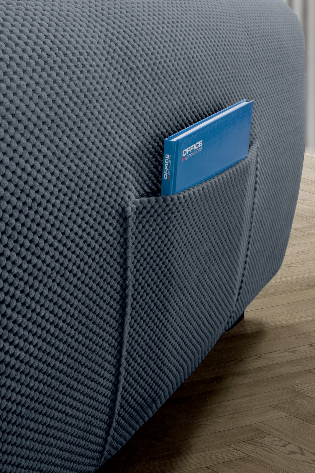 Close-up van een grijze, gestructureerde hoekbank met een handig zijvak waarin een blauw notitieboekje ligt. Zijaanzicht.
