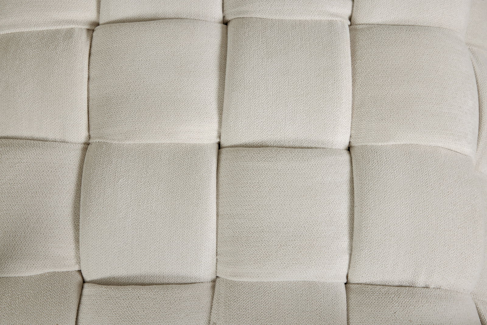 Nahaufnahme eines gepolsterten Hockers mit quadratischem Muster in cremefarbener Textur, von oben betrachtet.