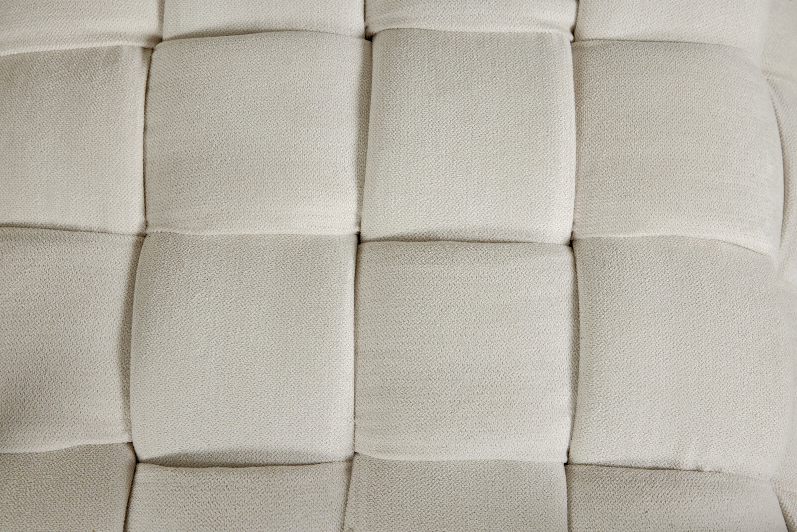 Nahaufnahme eines gepolsterten Hockers mit quadratischem Muster in cremefarbener Textur, von oben betrachtet.