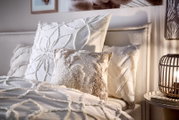 Close-up van een gezellig bed met sierkussens en een gestructureerde bontdeken in een stijlvol ingerichte slaapkamer.