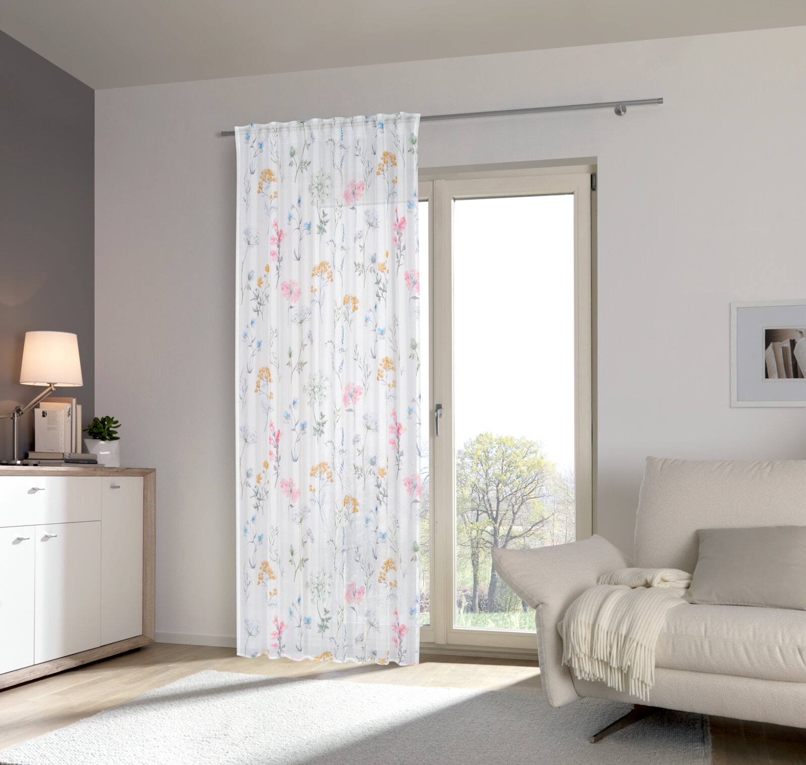 Esposa Fertigvorhang 135x145cm Halbtransparenter weißer Vorhang mit zartem Blumenmuster in Pastellfarben an einer Gardinenstange vor einer Balkontür, Innenraumansicht in Frontalperspektive.