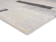 Nahaufnahme eines modernen Teppichs mit geometrischem Muster in Beige- und Grautönen, perspektivisch von der Seite aufgenommen.