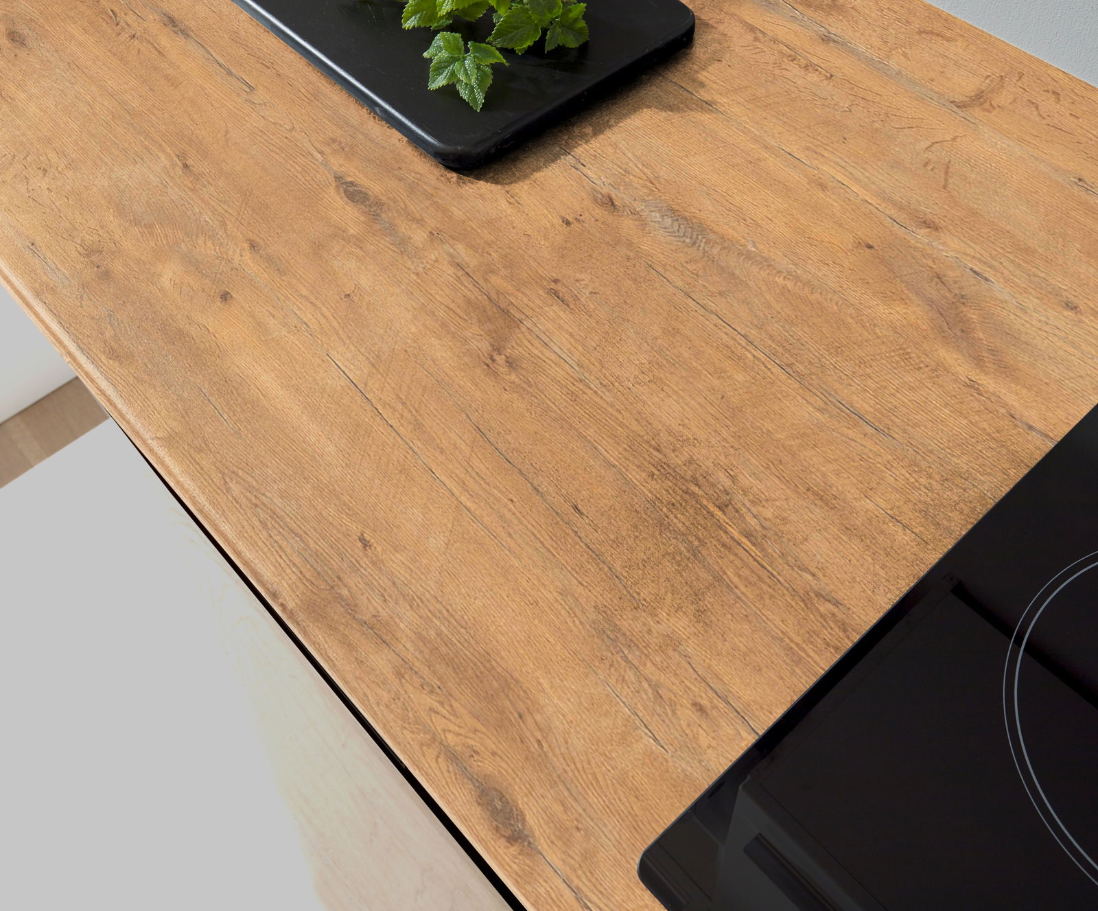 Holzarbeitsplatte einer Single-Küche mit schwarzem Kochfeld und Kräutern auf einem Tablett, aus der Vogelperspektive betrachtet.