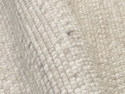 Nahaufnahme eines handgewebten Teppichs in cremefarbenen Tönen, die Textur und Webart sind deutlich sichtbar.