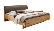 Modernes Doppelbett aus hellem Massivholz mit gepolstertem braunem Kopfteil und neutraler Bettwäsche, schräg von vorne links fotografiert
