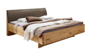 Modern tweepersoonsbed van licht massief hout met een bruin gestoffeerd hoofdeinde en neutraal beddengoed, schuin van linksvoor gefotografeerd