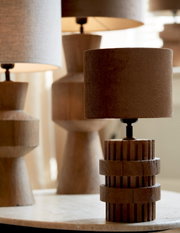 Nahaufnahme eines stilvollen Lampenschirms in Zylinderform auf einem Tisch, umgeben von weiteren Lampen im Hintergrund.