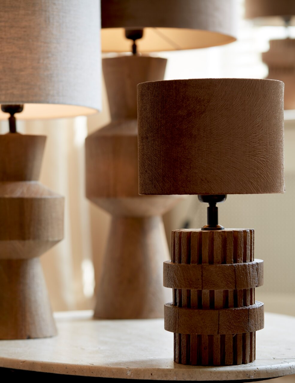 Nahaufnahme eines stilvollen Lampenschirms in Zylinderform auf einem Tisch, umgeben von weiteren Lampen im Hintergrund.