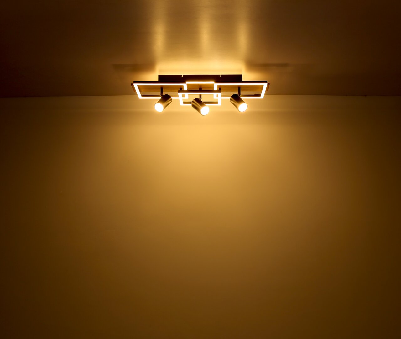 Moderne Deckenleuchte mit drei Strahlern, von unten betrachtet, die warmes Licht an die Decke und den Raum abgibt.