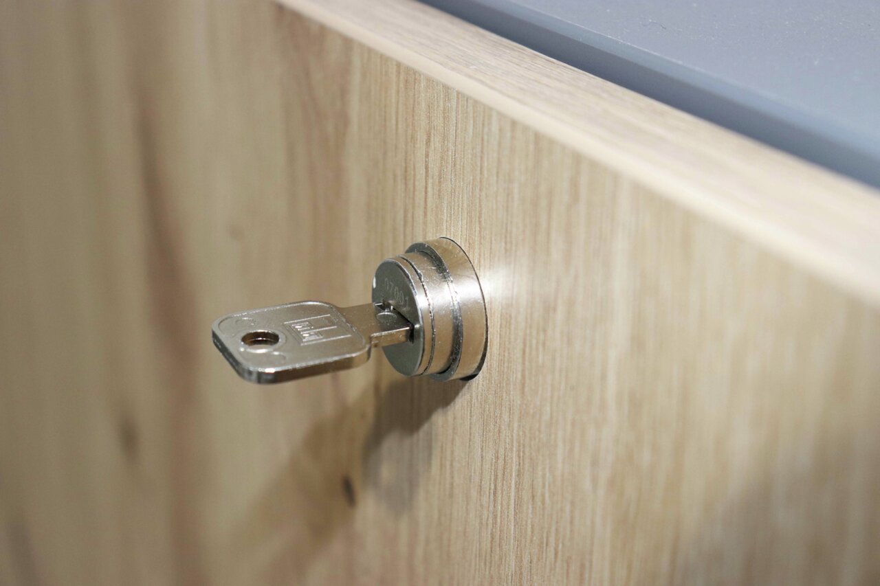 Close-up van een sleutel in een slot van een houten wandbureau, gezien vanuit de zijkant.